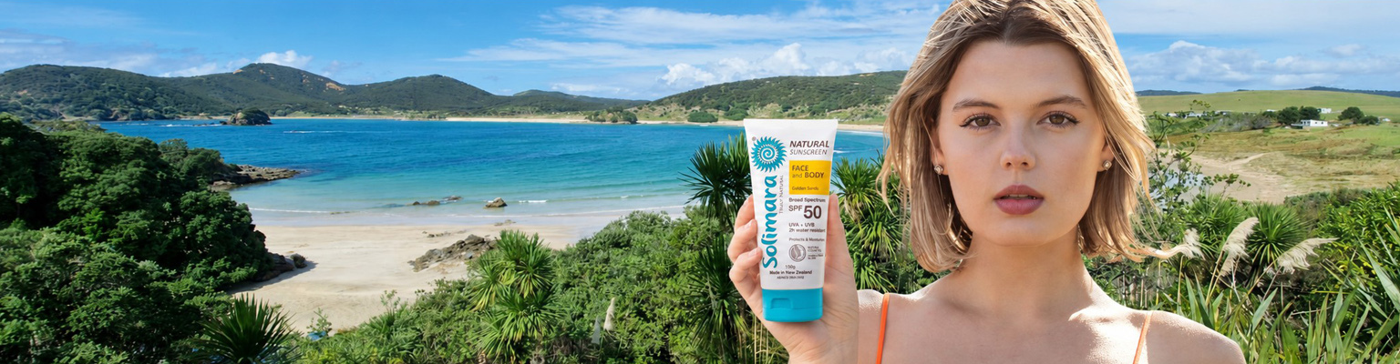 Woman on a sunny beach holding a tube of sunscreen SPF 50, with blue sea and green hills in the background, promoting sun protection.